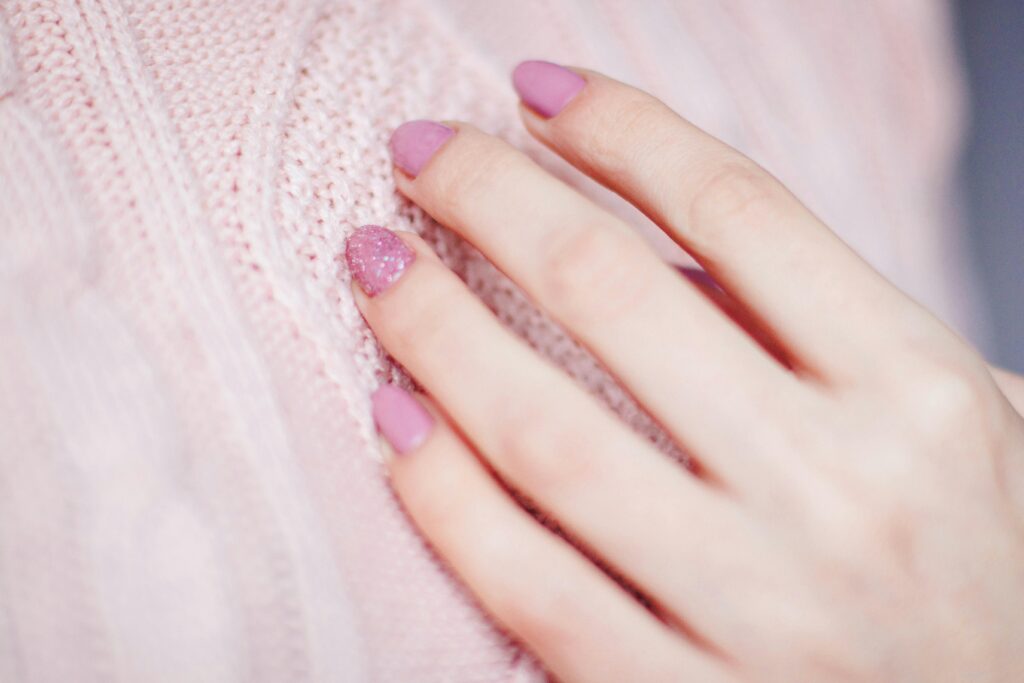 Close-up of a woman's hand with pink manicure resting on a soft knit sweater, showcasing elegance and fashion. lilac nail trend